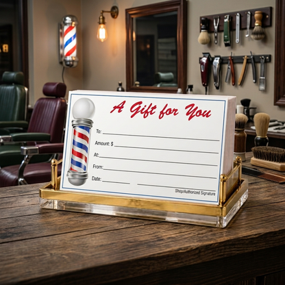 A barbershop-themed gift card holder and gift card set on a wooden counter inside a barbershop. The clear acrylic stand with gold-toned metal trim holds a white card printed with 'A Gift for You' in red script, a classic red, white, and blue barber pole g